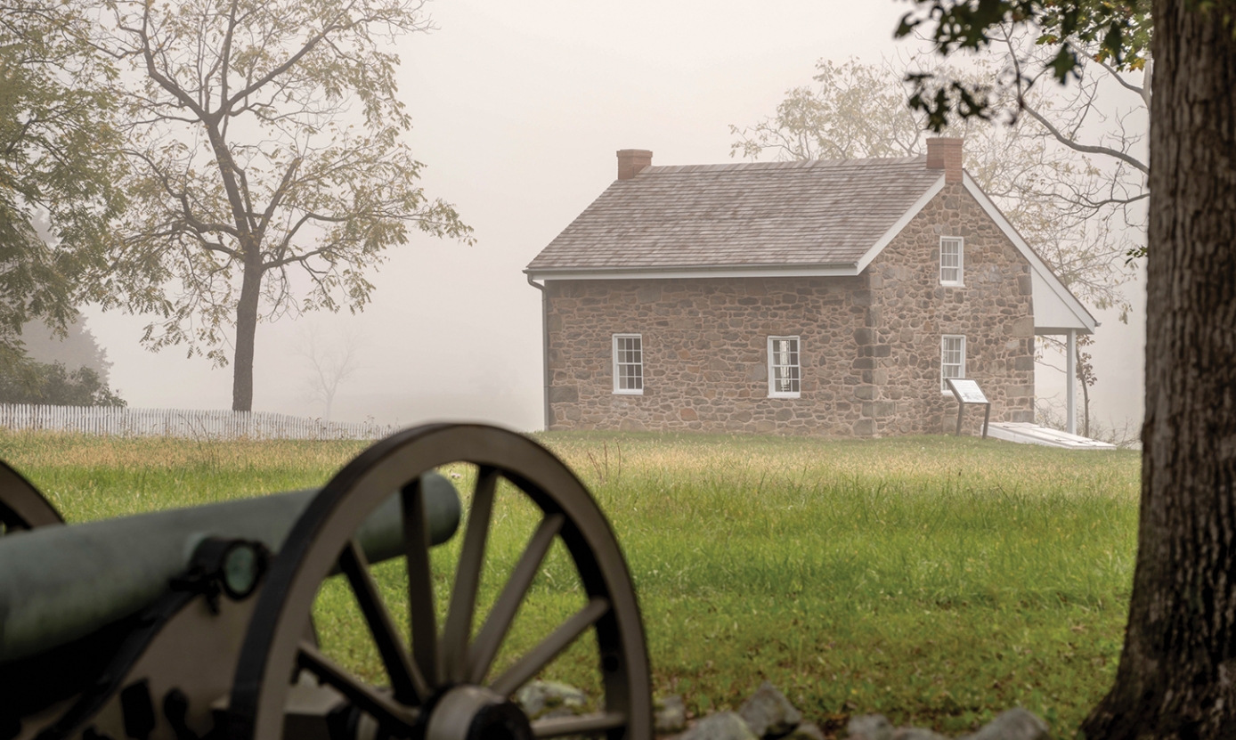 Looking across a field, through fog at the Warfield House with a canon in the foreground