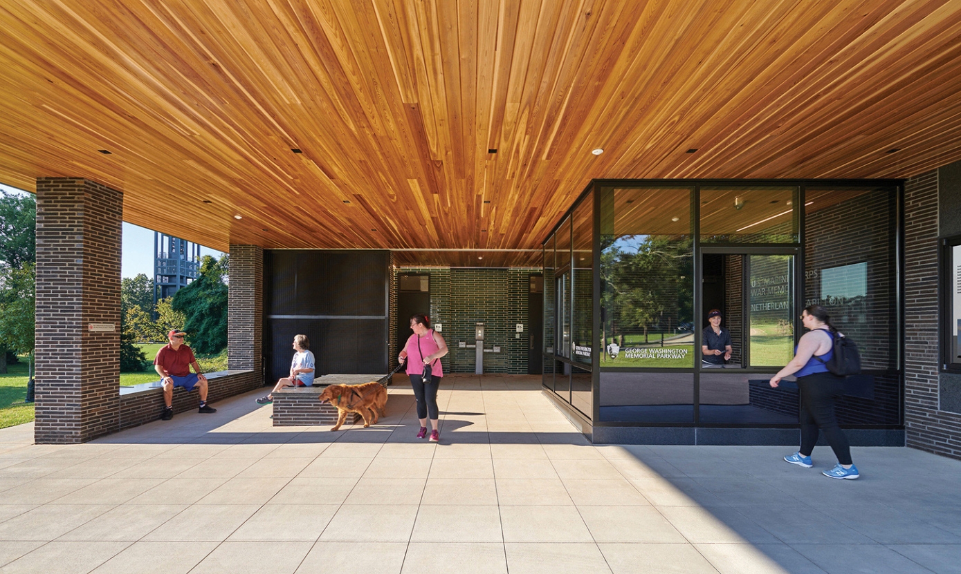 Covered entrance to the Comfort Station. Tiled patio, wood panel ceiling, people walking and sitting.
