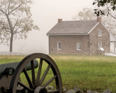 Looking across a field, through fog at the Warfield House with a canon in the foreground