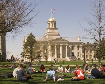 students sitting on campus lawn with Iowa State Capitol Building is the distance